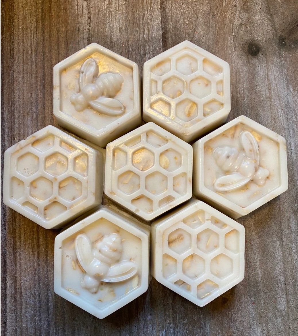 Seven cream-coloured hexagonal oat and beeswax soaps arranged on weathered wood