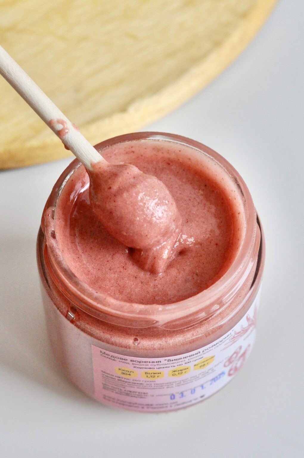 Open jar of pink cherry and rosemary whipped honey with a wooden dipper
