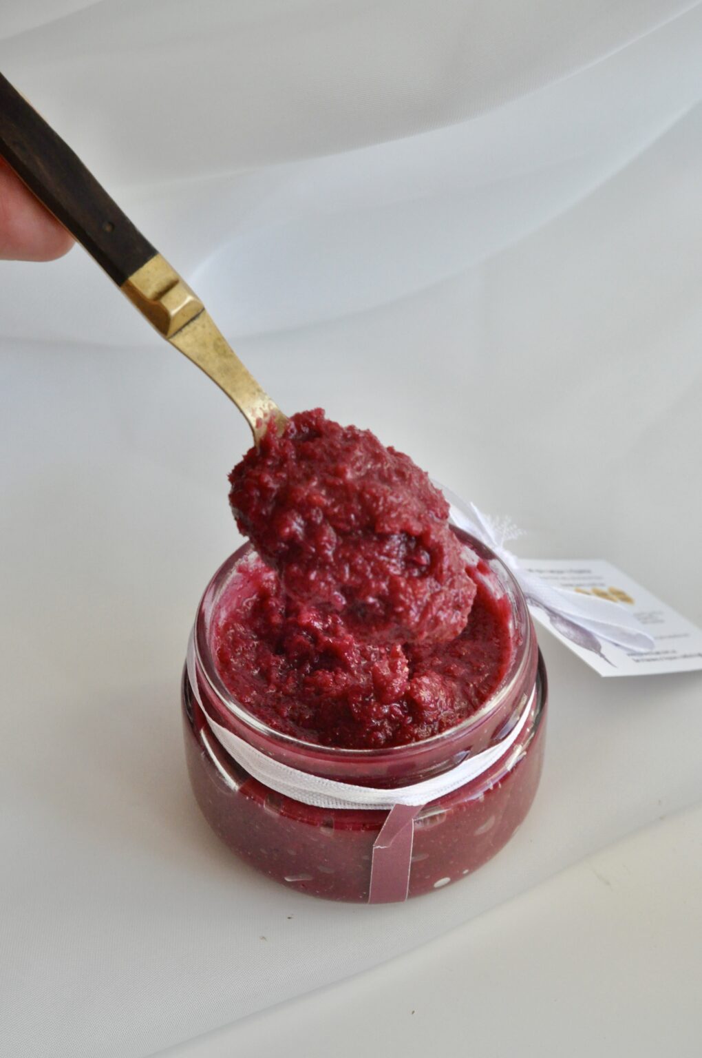 Deep red beetroot and horseradish honey relish being lifted from a glass jar