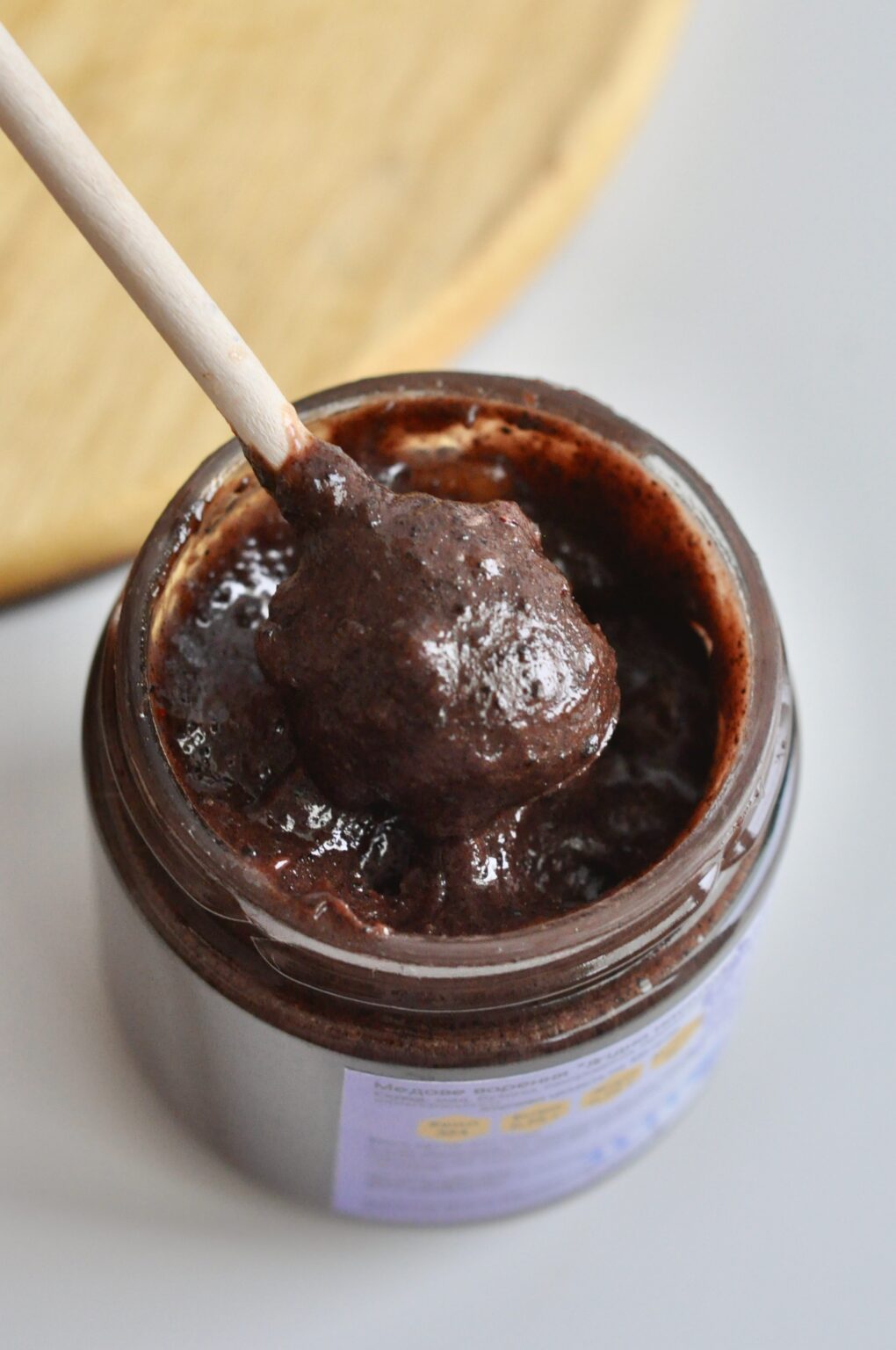 Dark cocoa cream honey on a wooden dipper above an open jar