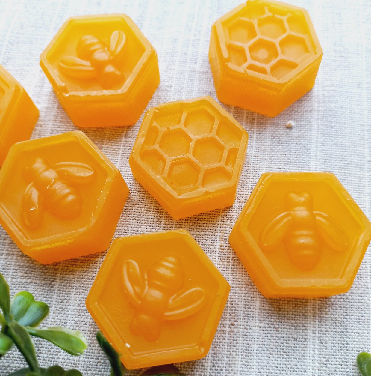 Six amber hexagonal glycerin soaps moulded with bee and honeycomb patterns on linen