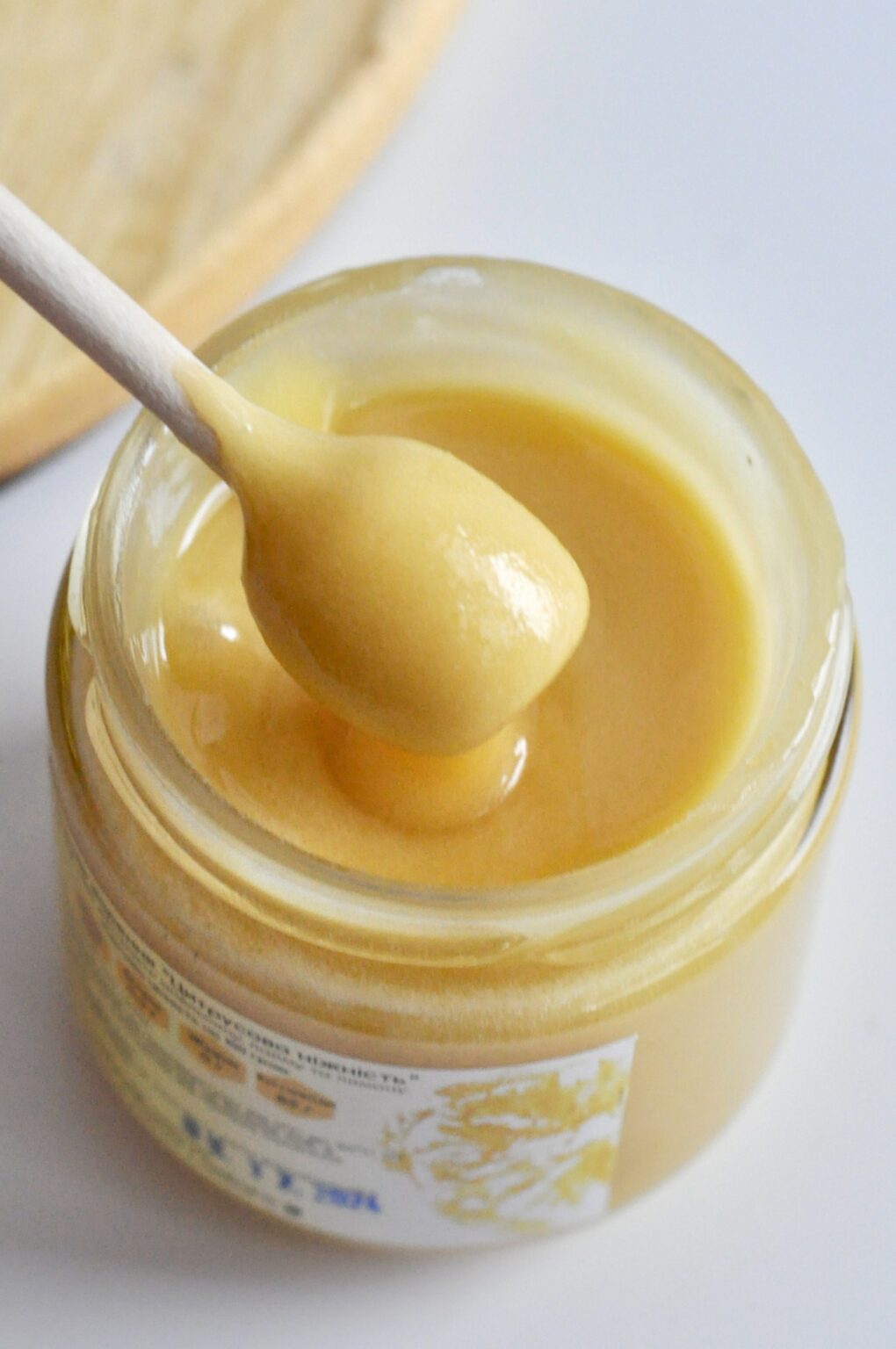 Smooth pale golden honey caramel cream in an open jar with a wooden spoon